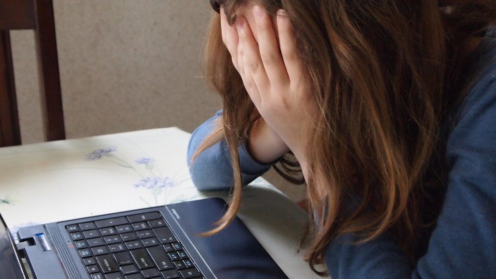 A girl with her head in her hands upset in front of an open laptop