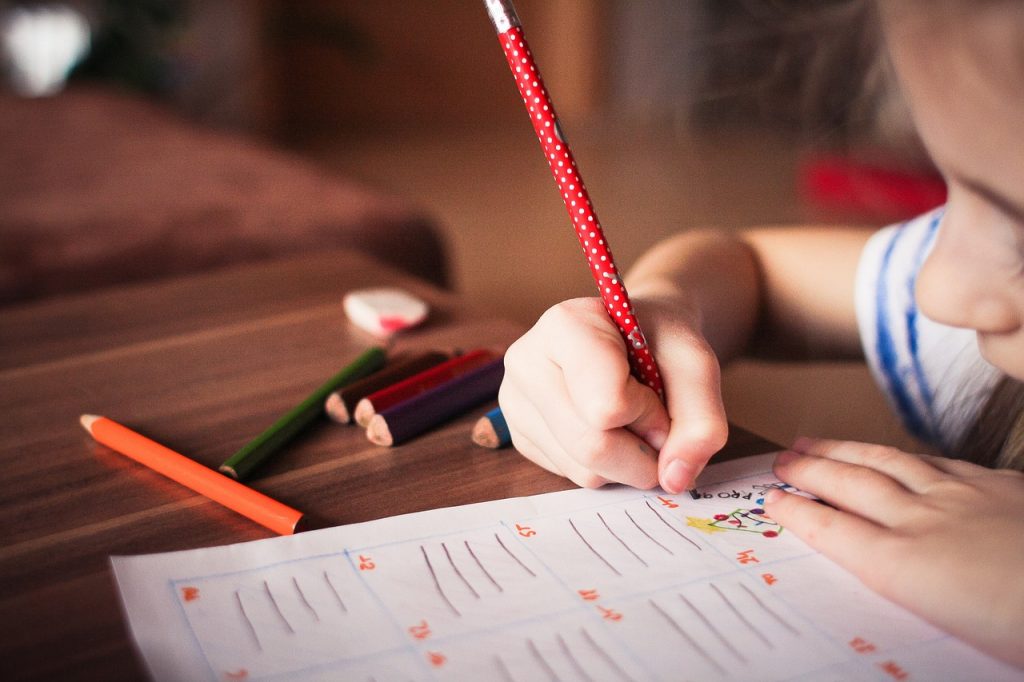 A girl writing school work using a red and white spotty pencil.