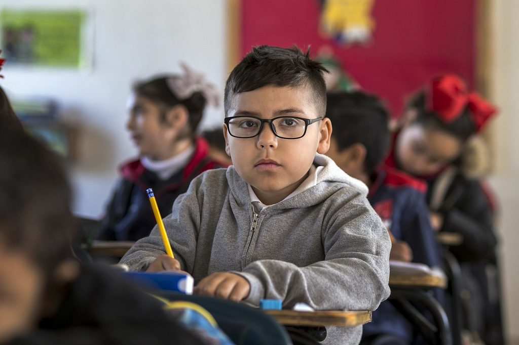A boy thinking in school writing using a yellow pencil